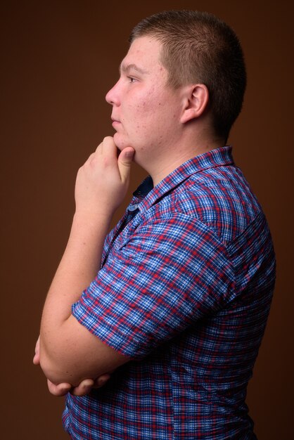 Studio shot of overweight young man wearing purple checkered shirt against brown background