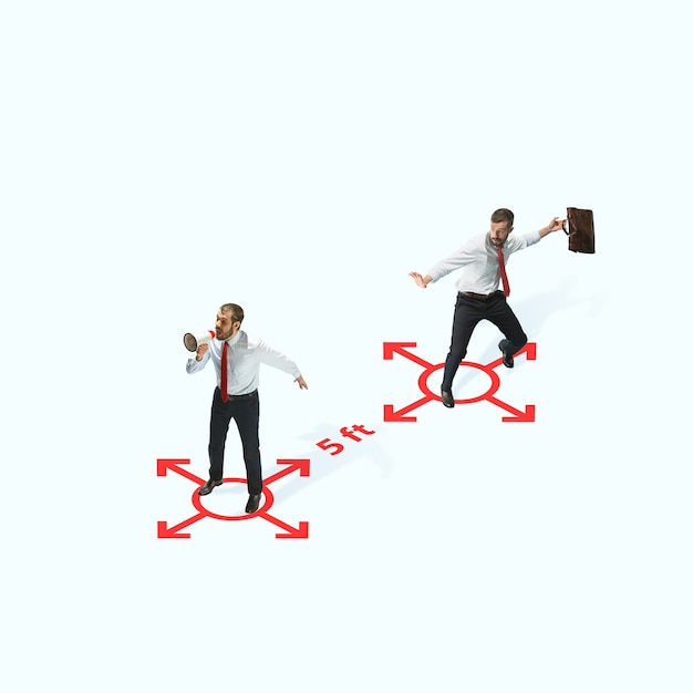 Studio shot of people demonstrating social distancing with arrows indicating the separation. Office workers during coronavirus outbreak with new rules for safety and healthcare. High angle view, copys