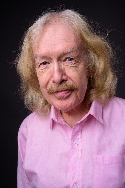 Studio shot of senior businessman with mustache wearing pink shirt against gray background