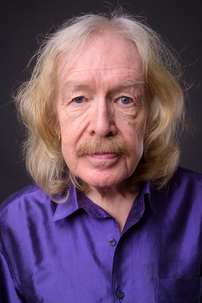 Photo studio shot of senior man with mustache wearing purple silky shirt against gray background