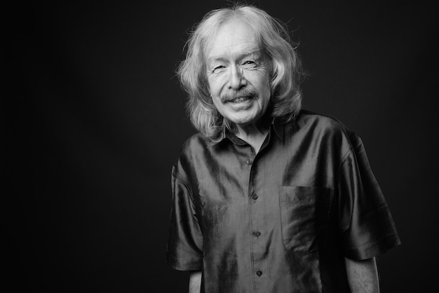 Studio shot of senior man with mustache wearing purple silky shirt against gray wall