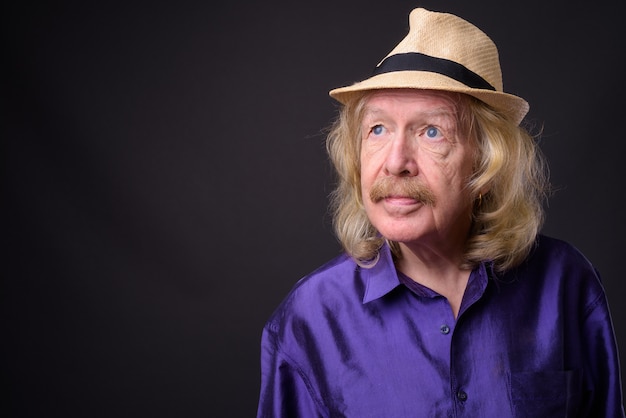 Studio shot of senior tourist man with mustache wearing hat against gray background