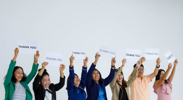 Photo studio shot of smiling male and female officer staff people group hold variety fonts thank you letters paper sign raised above head show appreciation gratitude to customers on white background.