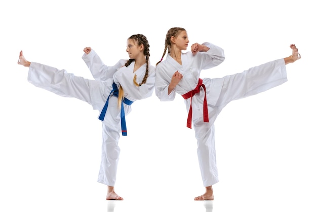 Studio shot of two teen girls, taekwondo athletes in uniform training isolated over white background