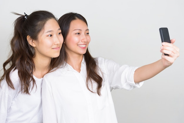Студийный снимок двух молодых красивых корейских женщин как друзей вместе на белом фоне