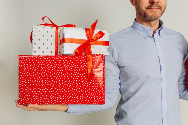 Studio shot of unrecognizable man in shirt is holding several gift boxes with red ribbons on his hand. Gifts for Christmas, Valentine's Day, Women's Day, Birthday, Mother's Day.