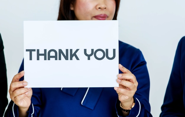 Studio shot of unrecognizable unidentified faceless female officer in business clothes holding thank you paper sign at chest showing appreciation to customers and colleagues on white background.