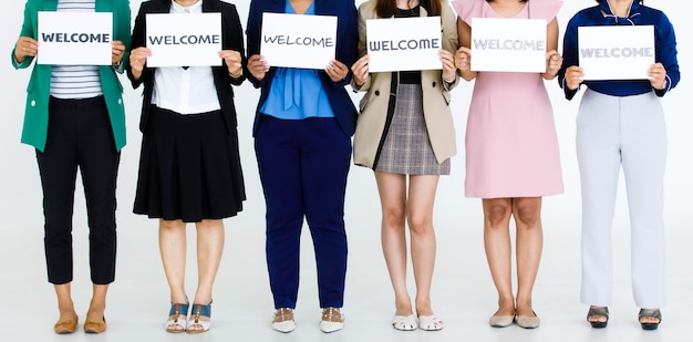 Studio shot of unrecognizable unidentified faceless female officer staff in business wears hold variety fonts welcome letters paper sign show warm greeting to customers colleagues on white background.