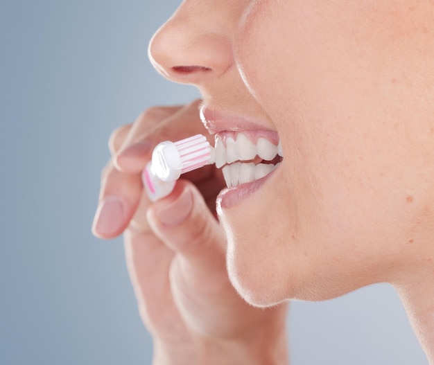 Студийный снимок неузнаваемой молодой женщины, чистящей зубы на сером фоне