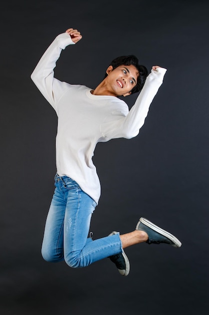 Studio shot van Aziatische jonge Lgbtq homo vrolijk gelukkig biseksueel homoseksueel mannelijk model in casual outfit springen hoog op lucht glimlachen lachen poseren met twee vingers vredesteken op zwarte achtergrond