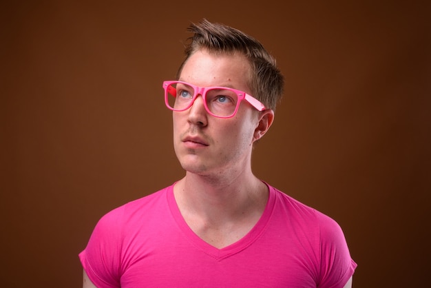 Studio shot van de jonge knappe man met roze shirt met bijpassende roze bril tegen bruine achtergrond