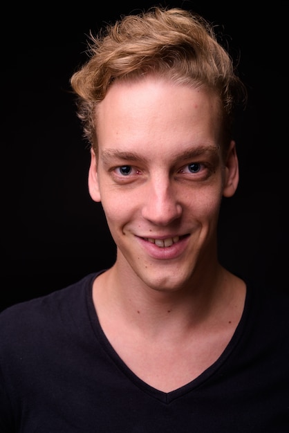 Studio shot van de jonge knappe Scandinavische man met blond haar tegen zwarte achtergrond