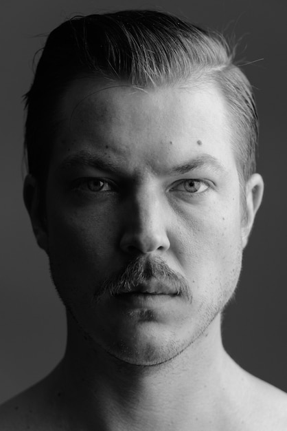 Studio shot van de jonge knappe Scandinavische man met snor shirtless tegen grijs in zwart-wit