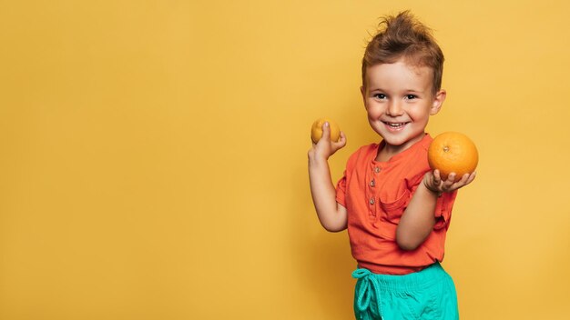 Studio shot van een lachende jongen met een verse citroen en sinaasappel op een gele achtergrond Het concept van gezonde babyvoeding vitaminen Een plek voor uw tekst