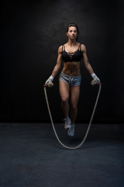 Studio shot van fit en gespierde vrouw met springtouw staande op zwart