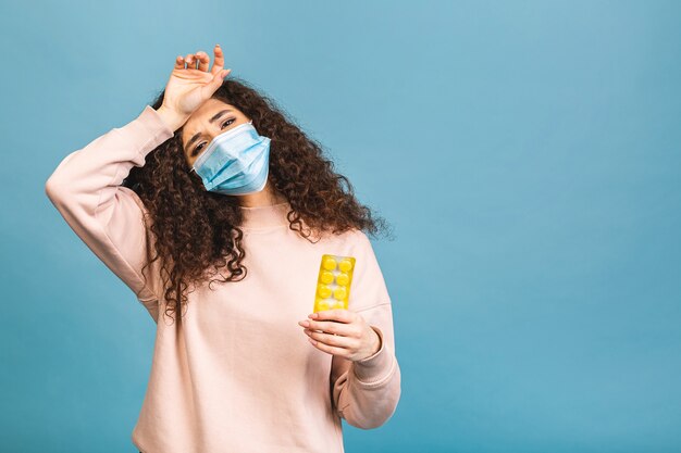 Studio shot van geïnfecteerde vrouw met pillen in handen, dame die beschermend gezichtsmasker draagt