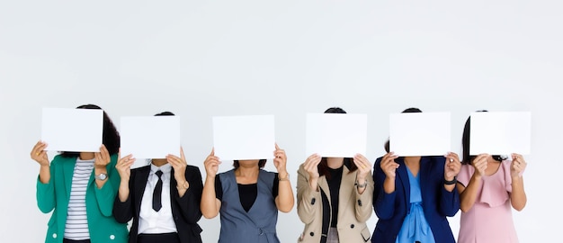 Studio shot van incognito niet-geïdentificeerde onherkenbare anonieme groep vrouwelijke kantoorpersoneel in het bedrijfsleven draagt stand hold leeg leeg papier teken dekking gezicht voor advertentie tekst op witte achtergrond.