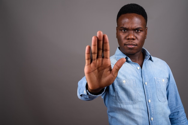 Studio shot van jonge Afrikaanse man met denim overhemd tegen een grijze achtergrond