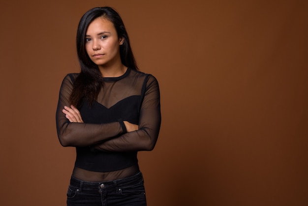 Studio shot van jonge Aziatische vrouw tegen bruine achtergrond