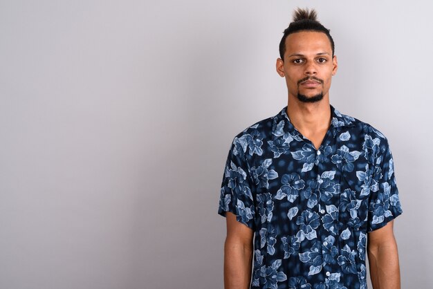 Studio shot van jonge bebaarde knappe Afrikaanse man met een Hawaiiaans shirt met haar vastgebonden tegen een grijze achtergrond