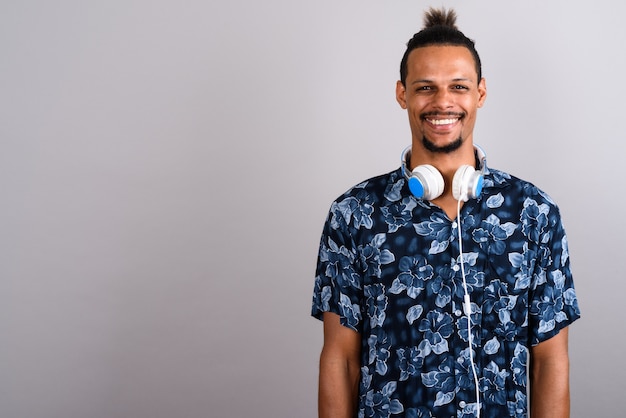 Studio shot van jonge bebaarde knappe Afrikaanse man met Hawaiian shirt en koptelefoon tegen een grijze achtergrond