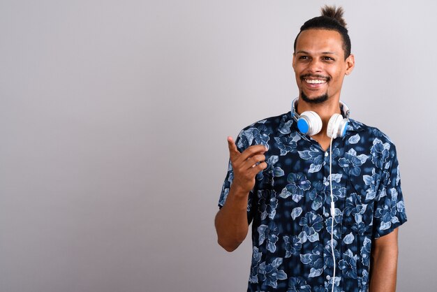 Studio shot van jonge bebaarde knappe Afrikaanse man met Hawaiian shirt en koptelefoon tegen een grijze achtergrond