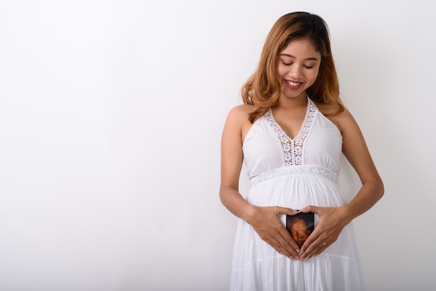 Studio shot van jonge gelukkige aziatische zwangere vrouw lachend en kijk