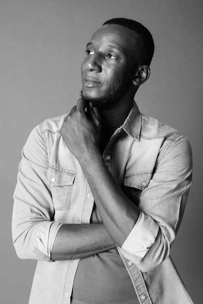 Studio shot van jonge knappe bebaarde Afrikaanse man met kort haar tegen grijs in zwart-wit