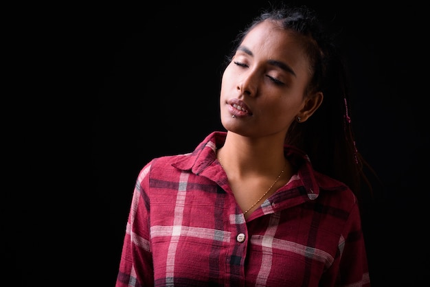 Studio shot van jonge mooie Aziatische hipster vrouw met gevlochten haar tegen zwarte achtergrond