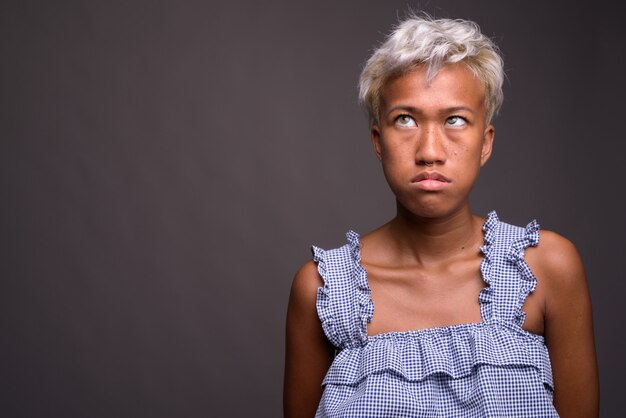 Foto studio shot van jonge mooie opstandige vrouw met kort haar tegen grijs