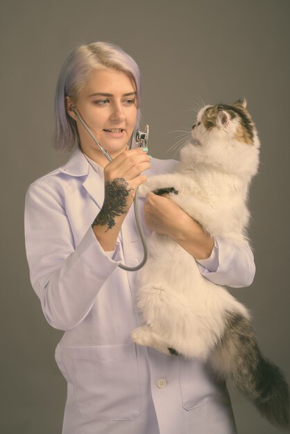 Studio shot van jonge mooie vrouw arts met kort kleurrijk haar op grijs