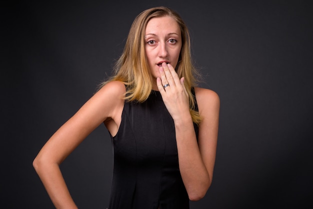 Studio shot van jonge mooie zakenvrouw met sluik blond haar tegen grijs