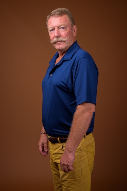 Studio shot van knappe senior man met snor blauw poloshirt dragen tegen bruin