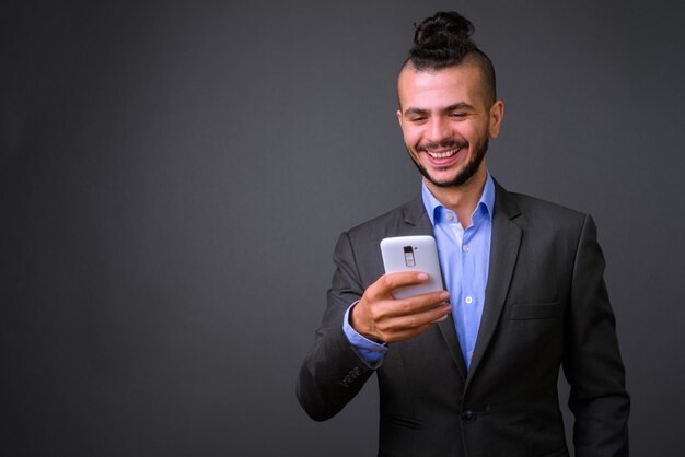 Studio shot van knappe turkse zakenman met behulp van mobiele telefoon tegen een grijze achtergrond