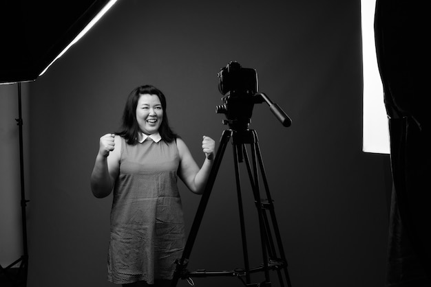 Studio shot van mooie dikke Aziatische vrouw, gekleed in jurk tegen een grijze achtergrond in zwart en wit