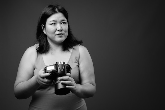 Studio shot van mooie dikke Aziatische vrouw, gekleed in mouwloze jurk tegen een grijze achtergrond in zwart en wit