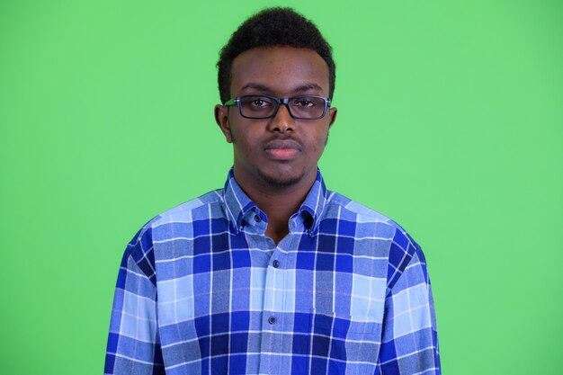 Studio shot of young African hipster man with Afro hair wearing eyeglasses against green background