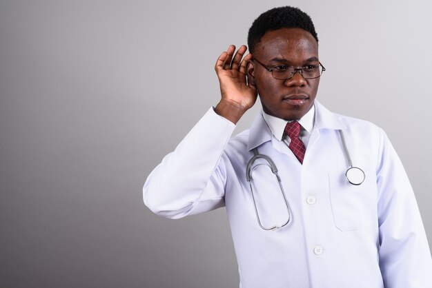Studio shot of young African man doctor wearing eyeglasses against white background