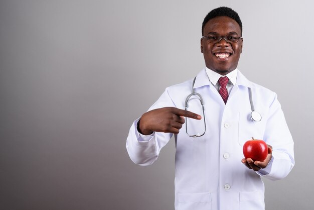 Studio shot di giovane uomo africano medico indossando occhiali da vista mentre si tiene la mela rossa su sfondo bianco