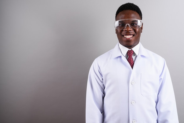 Studio shot of young African man doctor wearing protective eyeglasses against white background