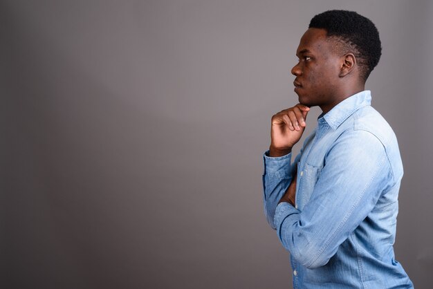 Studio shot of young African man wearing denim shirt against gray background