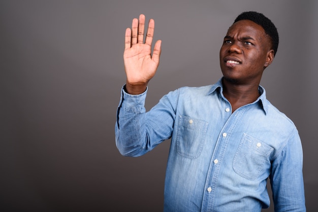 Studio shot del giovane africano che indossa la camicia in denim su sfondo grigio