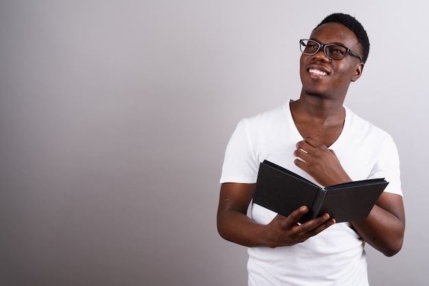 白い背景の本を読んでいる間眼鏡をかけている若いアフリカ人のスタジオショット