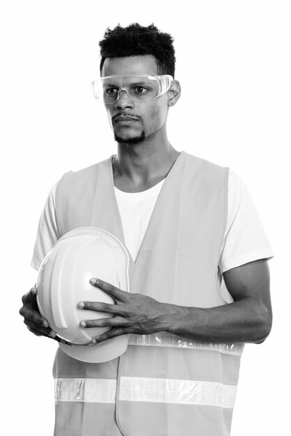 Studio shot of young bearded African man construction worker isolated against white background in black and white