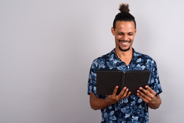 Studio shot of young bearded handsome African man reading book against gray background