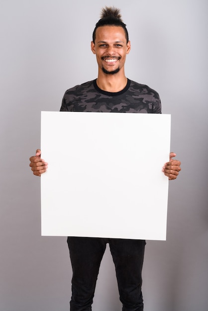 studio shot of young bearded handsome african man wearing camouflage printed shirt with hair tied against gray background