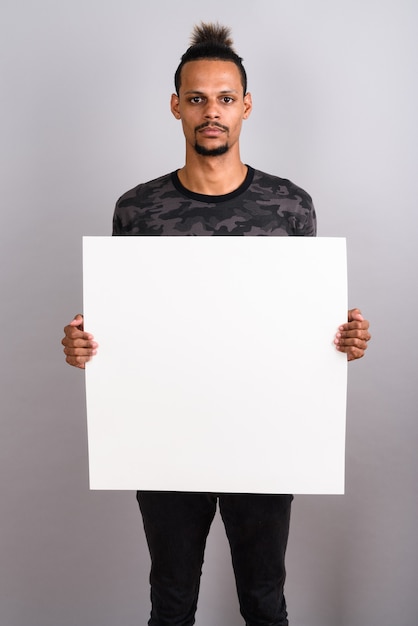 Studio shot of young bearded handsome African man wearing camouflage printed shirt with hair tied against gray background