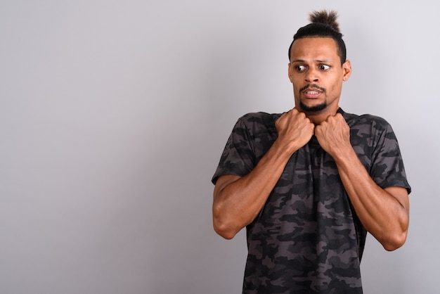 Studio shot of young bearded handsome African man wearing camouflage printed shirt with hair tied against gray background