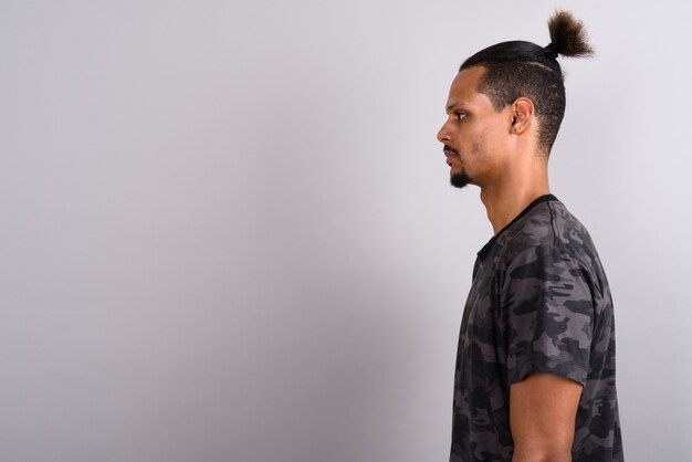 Studio shot of young bearded handsome African man wearing camouflage printed shirt with hair tied against gray background