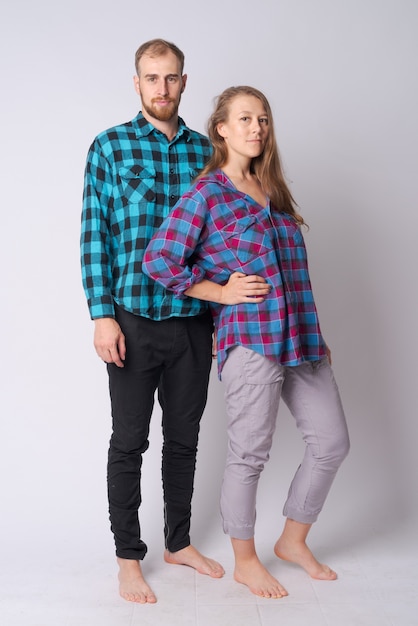 Studio shot of young bearded hipster man and young hipster woman together against white